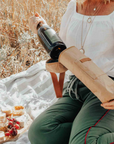 Person sitting outdoors with a picnic setup, getting wine from insulated brown wine tote bag