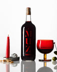 Partida Creus MUZ vermouth bottle with red glass, olives, and candle on reflective surface in Catalonia Spain for Mysa Natural Wine