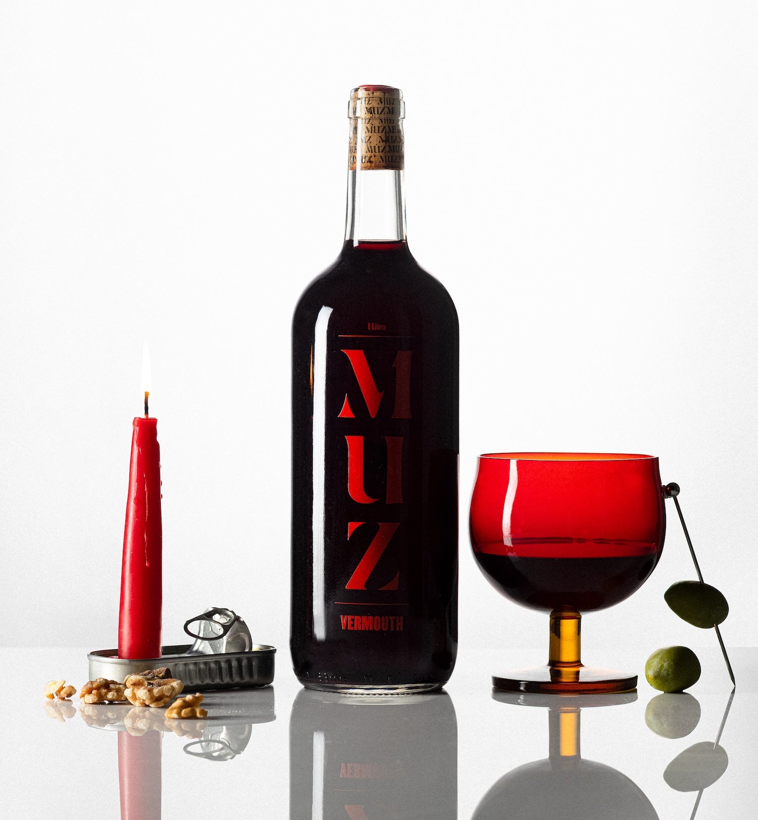 Partida Creus MUZ vermouth bottle with red glass, olives, and candle on reflective surface in Catalonia Spain for Mysa Natural Wine