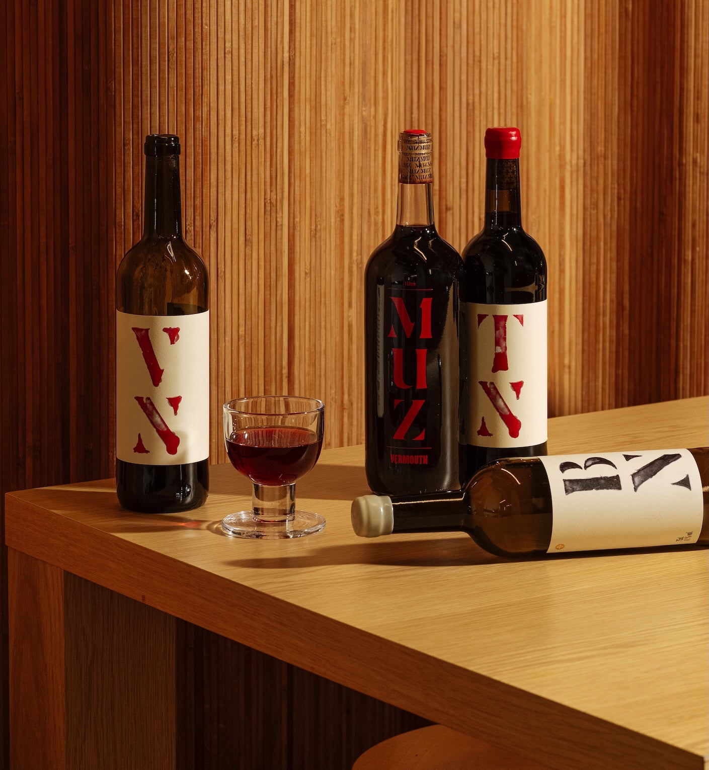 Partida Creus natural wine bottles including TN, VN, BN, and MUZ vermouth with glass on wooden table in Catalonia Spain for Mysa Natural Wine